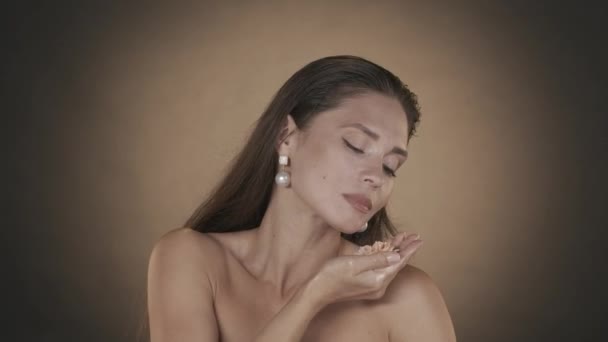 魅力的な女性の肖像画 メイクとイヤリングで女性モデルのクローズアップショット 女性はバラの花の匂いを嗅ぎ それを絞り 黄金の液体が彼女の手首によって流れ落ちる ビューティー広告コンセプト — ストック動画