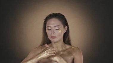 Güzel esmer bir kadının portresi. Yüzünde altın boya gözyaşları olan ve ellerindeki kuru altın boyayı soyan bir kadın modelin yakın plan fotoğrafı. Güzellik reklamı konsepti. HDR
