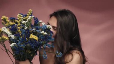 Bir kadın taze kır çiçeklerinin kokusunu içine çekiyor. Stüdyoda elinde bir buket kır çiçeğiyle pembe arka planda gezen bir kadın. Güzellik, kozmetoloji, bakım, spa, kadın sağlığı kavramı.