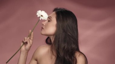 Bir kadın papatya çiçeğini yüzünün ve boynunun üstünde tutar. Stüdyoda pembe arka planda bir kadın var. Papatya çayı bazlı kozmetik ürünler rahatlatıcı, ferahlatıcı, nemlendirici, tonlama