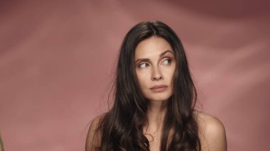 Pembe arka planda, gizemli, dalgın bir kadının portresi. Güzellik konsepti. Doğal güzellik, kozmetoloji, cilt bakımı.