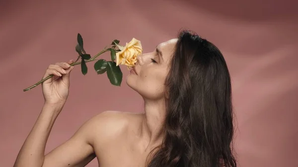 セミナーの女性は 長い茎の上に黄色いバラを保持し その香りを吸収します ピンクのバックグラウンドのスタジオにいる女性 春と夏のインスピレーション 化粧品のコンセプト — ストック写真