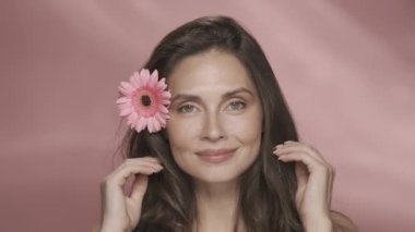 Bir kadın ona dokunarak saçından zevk alır. Stüdyoda pembe arka planda saçında Gerbera çiçeği olan bir kadının portresi. Kozmetik saç bakım ürünleri, özlü ve çiçek kokulu. Şey...