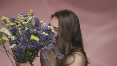 Bir kadın taze kır çiçeklerinin kokusunu içine çekiyor. Stüdyoda elinde bir buket kır çiçeğiyle pembe arka planda gezen bir kadın. Güzellik, kozmetoloji, bakım, spa, kadın sağlığı kavramı.