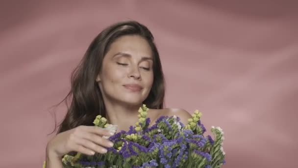 新鮮な野生の花束を持った女性 スタジオのセミノードの女性がピンクのバックグラウンドに近い 化粧品 女性の健康Hdr Bt2020 Hlg材料の概念 — ストック動画