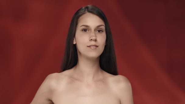 여자는 어깨의 피부를 만지고 화장품 효과를 즐깁니다 빨간색 배경에 스튜디오에서 — 비디오