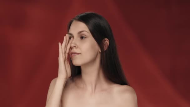 女性は目の下のきれいで滑らかな肌に触れます 赤い背景のセミナーの女性のプロフィール肖像画が閉じられています 自然の美しさ プラスチック手術 化粧品 ケアの概念 — ストック動画