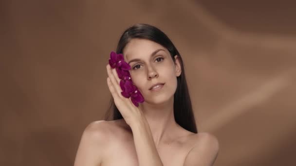 Ellerinde Orkide Çiçekleri Olan Bir Kadın Yüzüne Dokunuyor Pürüzsüz Yumuşak — Stok video