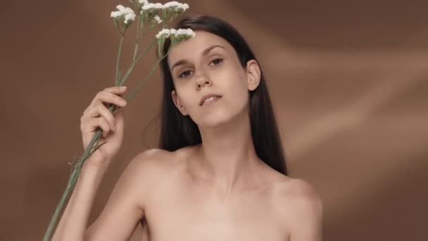 여자는 꽃으로 그녀의 얼굴을 만집니다 배경에 스튜디오에서 여자의 세미나의 초상화 — 비디오