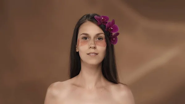 一个有着兰花和粉红水凝胶斑斑的有种子的女人的画像 工作室里一个棕色背景的女人美容美发的概念 — 图库照片