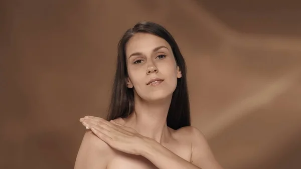 女性は肩の皮膚にクリームをこすります 茶色の背景にあるスタジオの若いセミナーの女性の肖像画 ケアのコンセプト — ストック写真