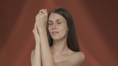 Bir kadın, stüdyoda ellerinin kadife gibi yumuşaklığından ve kırmızı arka planda olmasından hoşlanır. Güzellik, kozmetoloji, el bakımı HDR BT2020 HLG Malzeme.