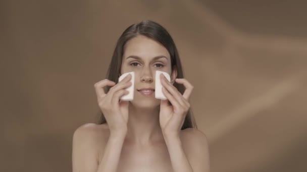 女人用棉垫来清洁她的脸 一个有着棕色背景的在工作室里的年轻女孩的画像 关怀的概念Hdr Bt2020 Hlg材料 — 图库视频影像