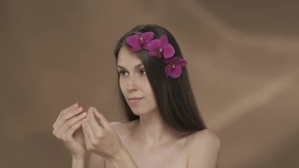 彼女の目の下にピンクのハイドロゲルパッチを塗った女性 茶色のバックグラウンドでスタジオで彼女の髪に蘭の花を持つセミナーの女性の肖像画 化粧品 スキンケアHdrのコンセプト — ストック動画