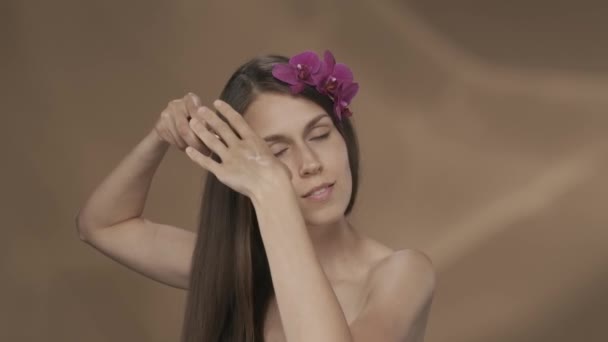 長い髪をかぶっている女性 スタジオで茶色の背景に彼女の髪に蘭の花を持つセミノードの女性 化粧品 ケアのコンセプト スローモーションHdr Bt2020 Hlg — ストック動画
