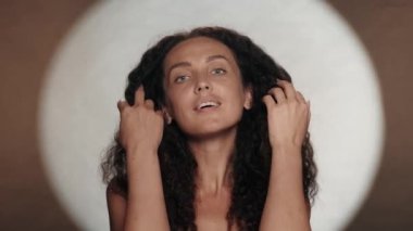 Turuncu arka planda beyaz dairesel ışığı olan örnek bir kadın. Rüzgarda çırpınan uzun kıvırcık saçlı bir kadın. Güzellik konsepti, saç stili, özen.
