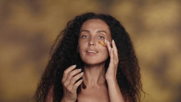 Długowłosa Brunetka Wykonuje Zabiegi Kosmetyczne Nakłada Złote Plamy Skórę Pod — Wideo stockowe