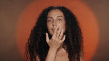 Kadın dudaklarına dokunuyor, merhem sürüyor ya da dudaklarına krem sürüyor. Stüdyoda, turuncu arka planda dairesel ışıklı bir kadının portresi. Güzellik konsepti, kozmetoloji, cilt bakımı