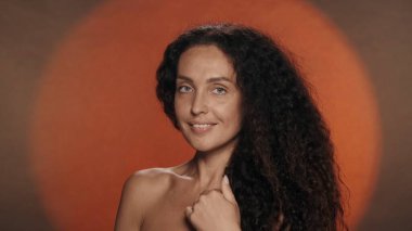 Normal hatları ve mükemmel cildi olan bir seminer kadınının portresi. Turuncu arka planda dairesel ışığı olan kıvırcık kadın stüdyoda. Yüz geliştirme. Doğal güzellik kavramı