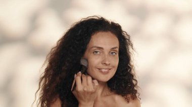 Makyaj fırçasıyla makyaj yapan bir kadın. Stüdyoda sarı arka planda, yakın planda bir seminer kadınının portresi. Konturing. Güzellik konsepti, kozmetoloji, cilt bakımı