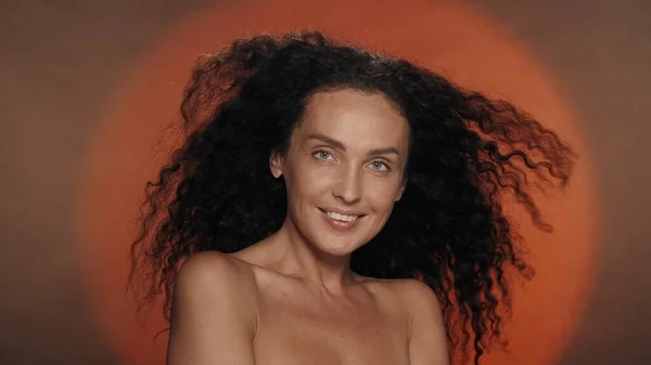 円形の光を持つオレンジ色の背景にあるセミノードの女性 長い曲がった髪の女性が風に揺れている ヘアスタイリング ケアのコンセプト — ストック写真