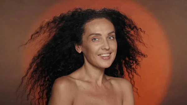 円形の光を持つオレンジ色の背景にあるセミノードの女性 長い曲がった髪の女性が風に揺れている ヘアスタイリング ケアのコンセプト — ストック写真