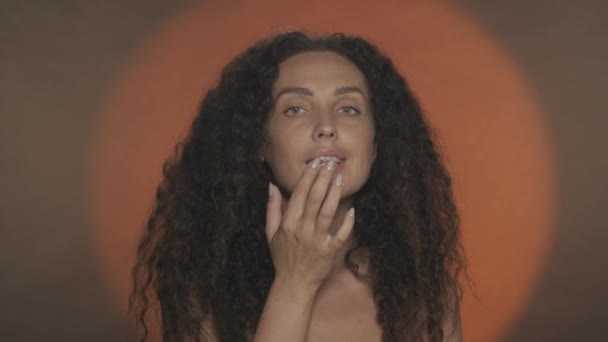 女性は唇にバームやクリームを塗り 空気のキスを送ります オレンジ色の背景にあるスタジオのセミナーの女性の肖像画 スキンケアのコンセプト — ストック動画