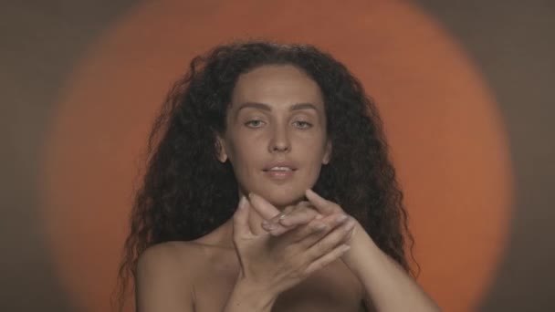 ハンドケアと保護 女性は彼女の手にスキンケアクリームを適用し 保湿します 円形の光でオレンジ色のバックグラウンドにスタジオでセミナーカーリー女性の肖像画 コンセプト — ストック動画