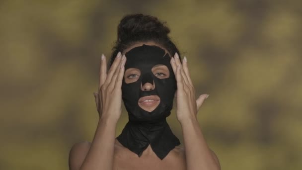 검은색 화장품 마스크를 여성과 머리에 뭉치가 하이라이트와 노란색 배경에 스튜디오에서 — 비디오