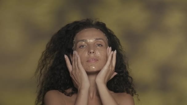 女性は彼女の顔から化粧水ゲル シリコーンマスクを取り除き 保湿された滑らかな肌に触れます ハイライト付きの黄色の背景にあるスタジオで笑顔のセミナーの女性の肖像画 イギリス — ストック動画