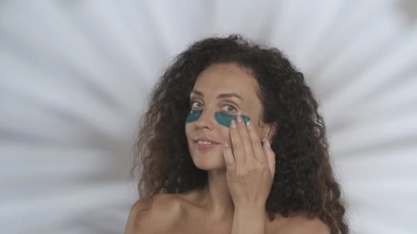 女性が修正し 目の下の青いヒドロゲルパッチを滑らかにします ハイライトのあるグレーの背景にあるスタジオのセミノードの女性 ビューティー 化粧品 スキンケアHdr Bt2020 Hlg材料 — ストック動画