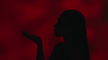 Avucundaki tüyleri uçuran genç bir kadın siluetinin yakın profil fotoğrafını çek. Koyu kırmızı arka plan. Boş zaman ya da ürün reklamı.