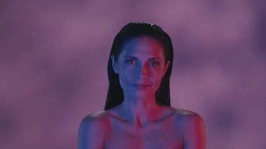 Genç bir kadının yüzünü yakından çek. O, neon pembe ve mavi renk şeması ile neşeli, flörtçü ve çekici bir şekilde kameraya güvenle bakıyor. Boş zaman ya da ürün reklamı.