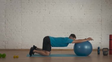Evde kişisel spor eğitimleri. Atletik erkek fitness koçu çevrimiçi dersler için ev stüdyosunda egzersiz yapıyor. Spor kıyafetli bir adam spor topunu geriyor. Sağlık hizmetleri kavramı.