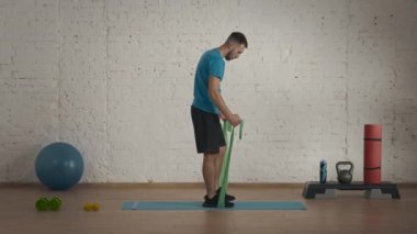 Evde kişisel spor eğitimleri. Atletik erkek fitness koçu çevrimiçi dersler için ev stüdyosunda egzersiz yapıyor. Spor giysili bir adam yarım yamalak lastik egzersizi yapıyor. Sağlık hizmetleri kavramı.