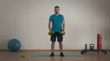Evde kişisel spor eğitimleri. Atletik erkek fitness koçu çevrimiçi dersler için ev stüdyosunda egzersiz yapıyor. Spor kıyafetli bir adam halterle kol kaldırma egzersizi yapıyor. Sağlık hizmetleri kavramı.