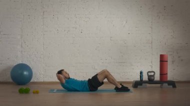 Atletik erkek fitness koçu çevrimiçi dersler için ev stüdyosunda egzersiz yapıyor. Spor kıyafetli bir adam klasik karın kasları egzersizi yapıyor. Sağlık hizmetleri kavramı.