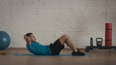 Yakın plan çekim. Atletik erkek fitness koçu çevrimiçi dersler için ev stüdyosunda egzersiz yapıyor. Spor kıyafetli bir adam klasik karın kasları egzersizi yapıyor. Sağlık hizmetleri kavramı.