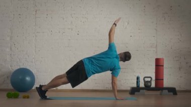Yakın plan çekim. Evde kişisel spor eğitimleri. Atletik erkek fitness koçu çevrimiçi dersler için ev stüdyosunda egzersiz yapıyor. Spor kıyafetli adam aktif, dirsek tahtası egzersizi yapıyor..