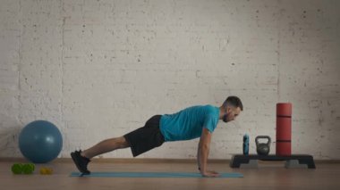 Evde kişisel spor eğitimleri. Atletik erkek fitness koçu çevrimiçi dersler için ev stüdyosunda egzersiz yapıyor. Spor kıyafetli bir adam düz kollar üzerinde statik tahta yapıyor..