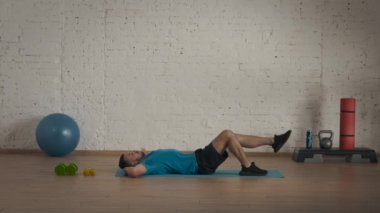 Spor iç mekanda. Atletik erkek fitness koçu çevrimiçi dersler için ev stüdyosunda egzersiz yapıyor. Spor kıyafetli bir adam vücut kasları egzersizi yapıyor. Sağlık hizmetleri kavramı.