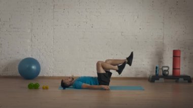 Atletik erkek fitness koçu çevrimiçi dersler için ev stüdyosunda egzersiz yapıyor. Spor kıyafetli bir adam bacak kası egzersizi yapıyor. Sağlık sigortası konsepti. Spor iç mekanda.