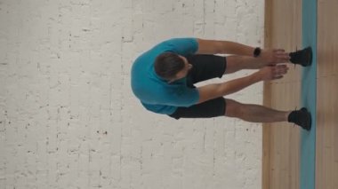 Dikey video. Evde kişisel spor eğitimleri. Atletik erkek fitness koçu çevrimiçi dersler için ev stüdyosunda egzersiz yapıyor. Spor kıyafetli bir adam ısınmak için geriniyor..