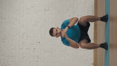 Dikey video. Evde kişisel spor eğitimleri. Atletik erkek fitness koçu çevrimiçi dersler için ev stüdyosunda egzersiz yapıyor. Spor kıyafetli bir adam standart basit çömelmeler yapıyor..