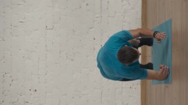 Dikey video. Evde kişisel spor eğitimleri. Atletik erkek fitness koçu çevrimiçi dersler için ev stüdyosunda egzersiz yapıyor. Spor kıyafetli bir adam esneyerek aktif kalas egzersizi yapıyor..