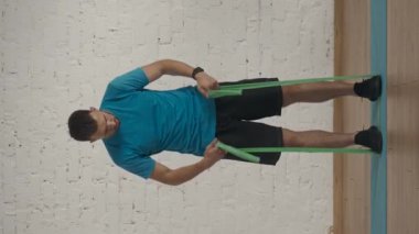 Dikey video. Evde kişisel spor eğitimleri. Atletik erkek fitness koçu çevrimiçi dersler için ev stüdyosunda egzersiz yapıyor. Spor kıyafetli bir adam göğüs lastiği egzersizi yapıyor..