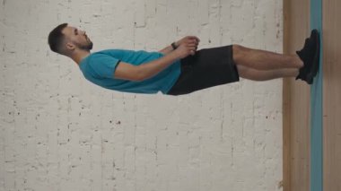 Dikey video. Yan görüş. Atletik erkek fitness koçu çevrimiçi dersler için ev stüdyosunda egzersiz yapıyor. Spor kıyafetli bir adam çapraz atlama egzersizi yapıyor. Sağlık hizmetleri kavramı.