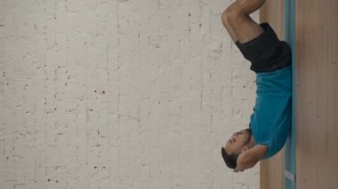 Dikey video. Atletik erkek fitness koçu çevrimiçi dersler için ev stüdyosunda egzersiz yapıyor. Spor kıyafetli bir adam klasik karın kasları egzersizi yapıyor. Sağlık hizmetleri kavramı.