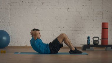 Yakın plan çekim. Spor jimnastik koçu çevrimiçi dersler için ev stüdyoda egzersiz yapıyor. Adam klasik karın kasları egzersizi yapıyor..