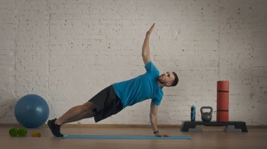 Yakın plan çekim. Spor jimnastik koçu çevrimiçi dersler için ev stüdyoda egzersiz yapıyor. Adam esneyerek dirsek egzersizi yapıyor..